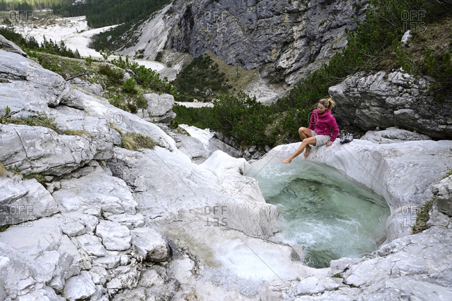 Mature female tourist sitting on rock while splashing water in stream