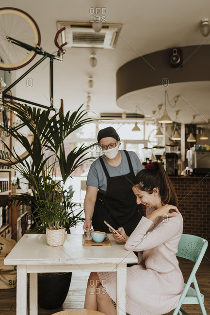 Waitress with protective mask serving Cappuccino in a coffee shop