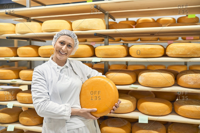Cheese factory- smiling female worker holding cheese wheel