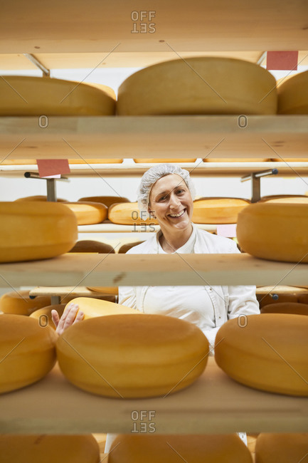 Cheese factory- female worker with cheese wheel in storeroom