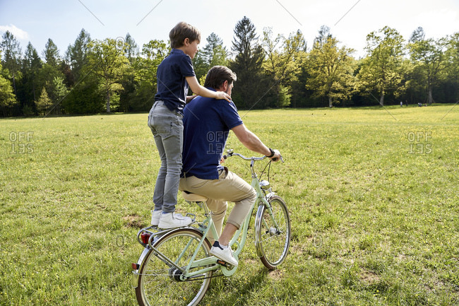 Father and son enjoying bicycle ride on grass during sunny day