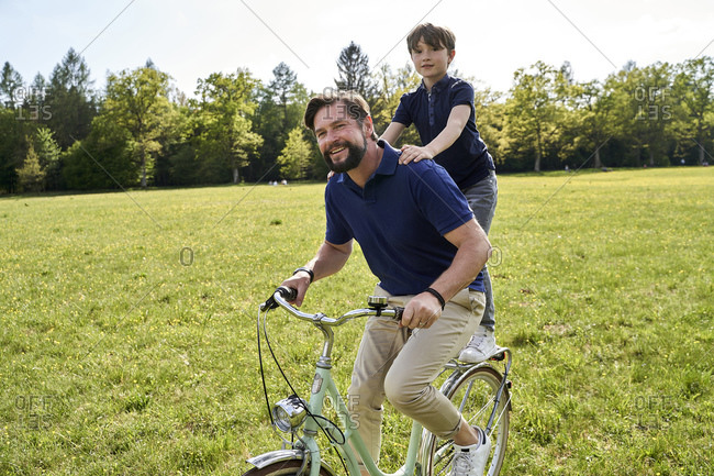Smiling father and son enjoying bicycle ride on grass during sunny day