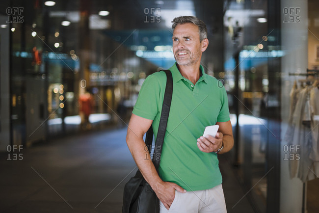 Smiling mature man looking away while using smart phone in shopping mall