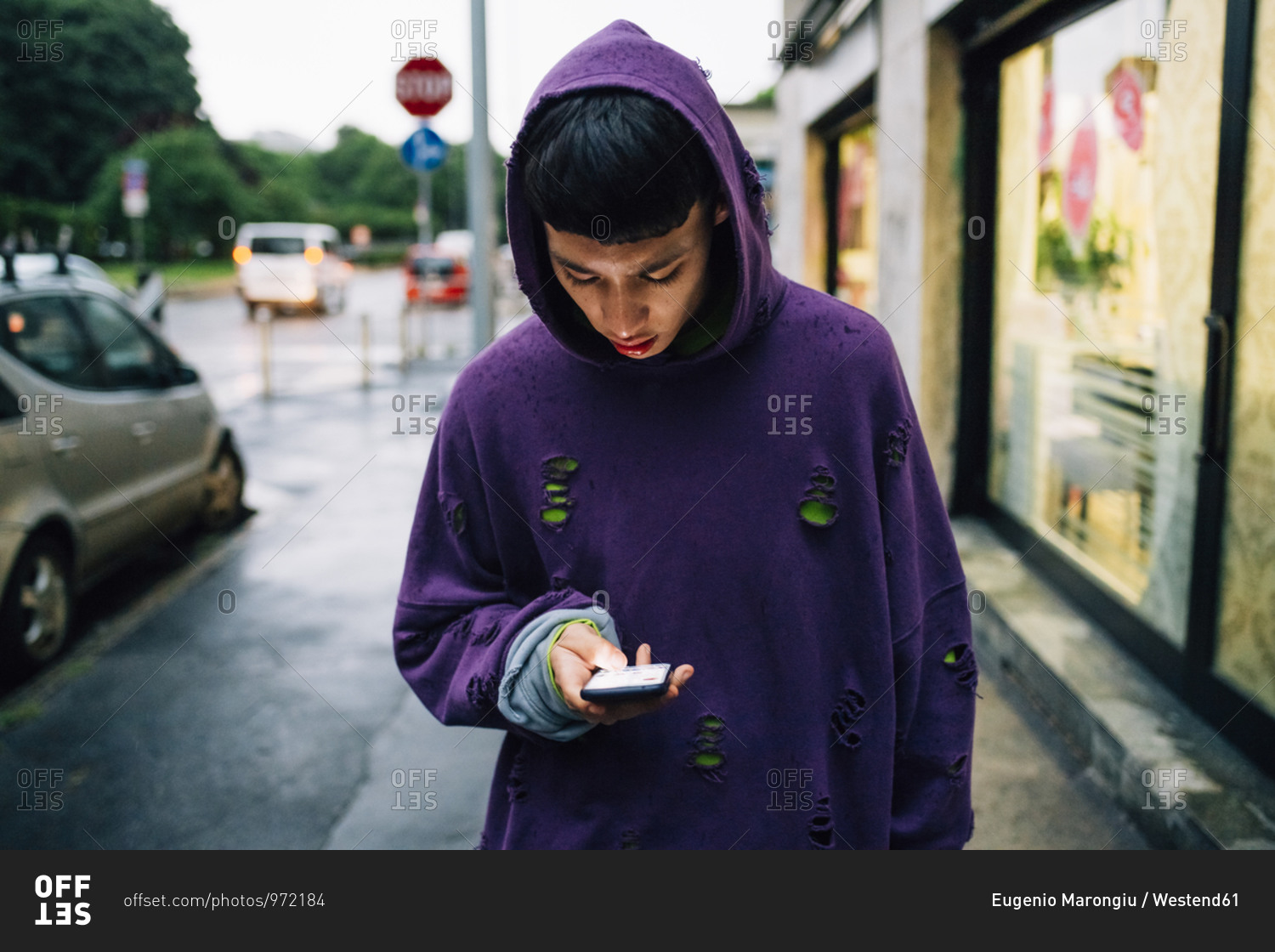 Young man wearing hooded shirt using smart phone while standing on street