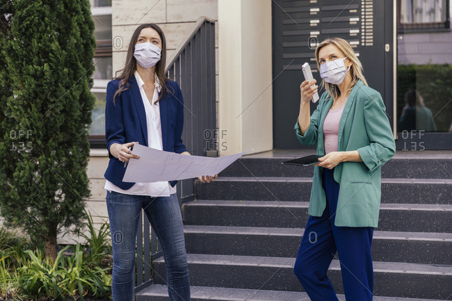Two real estate agents wearing face masks while inspection outdoor area of house
