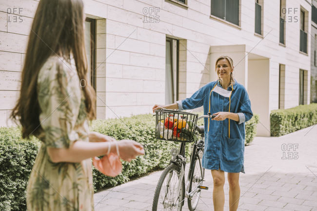 Two women with bicycle and face mask meeting in urban area