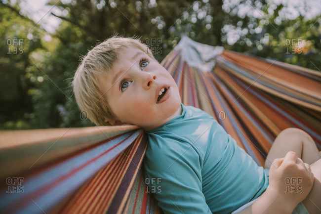 Cute boy looking up while relaxing on hammock at garden during sunny day