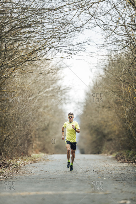 Young male athlete running on country road amidst bare trees