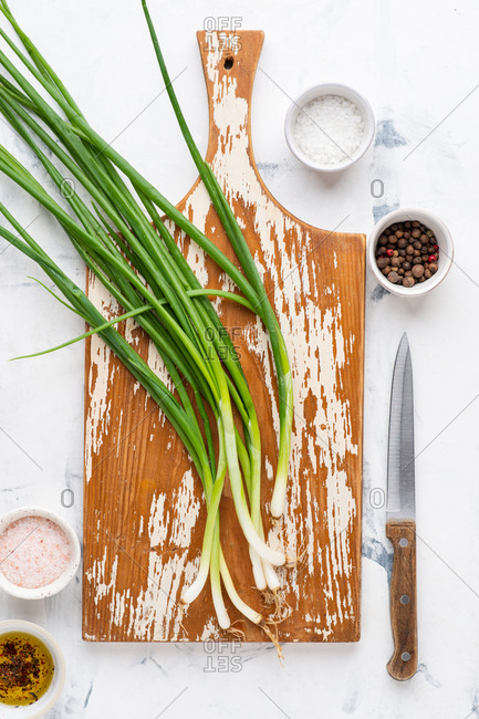 Spring onion on wooden cutting board and small ceramic bowls with various spices over white background viewed from above