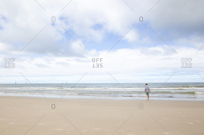 Rear view of boy dipping his feet in the ocean tide