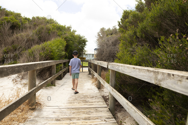 Boy walking on sandy boardwalk