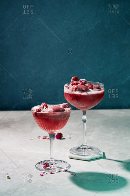 Pink cocktails garnished with raspberries and sorbet on a moody backdrop