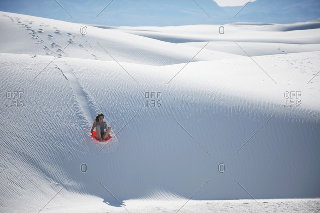 Woman sledding down sand dune, White Sands National Monument, New Mexico, USA