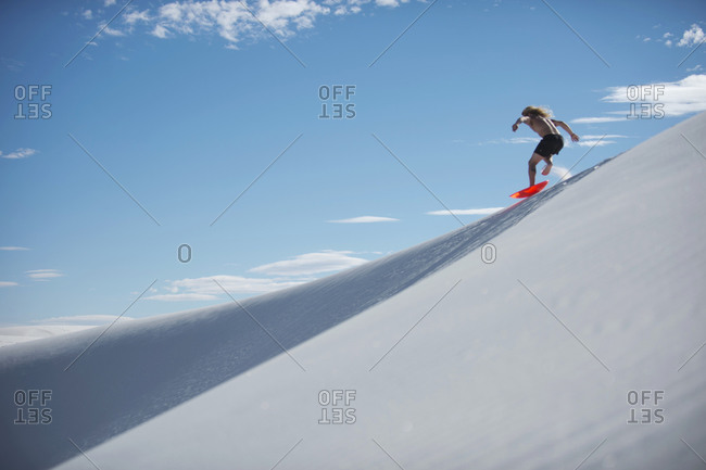 Man sledding down sand dune, White Sands National Monument, New Mexico, USA