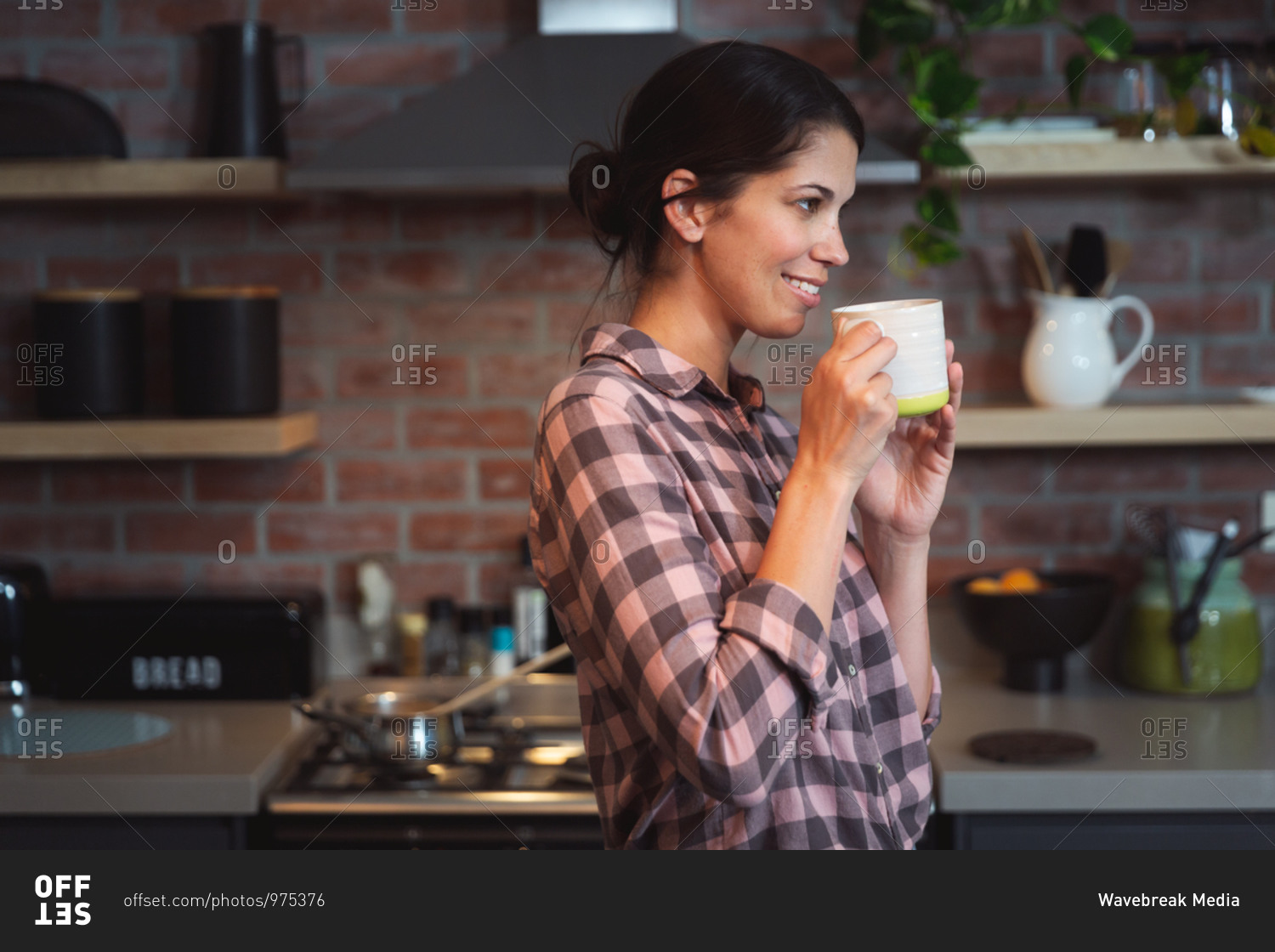 Mixed race woman spending time at home self isolating and social distancing in quarantine lockdown during coronavirus covid 19 epidemic, holding a mug of coffee in kitchen.
