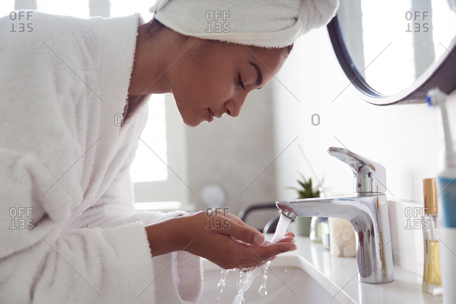 Mixed race woman spending time at home self isolating and social distancing in quarantine lockdown during coronavirus covid 19 epidemic, wearing bathrobe with towel on her head washing in bathroom.