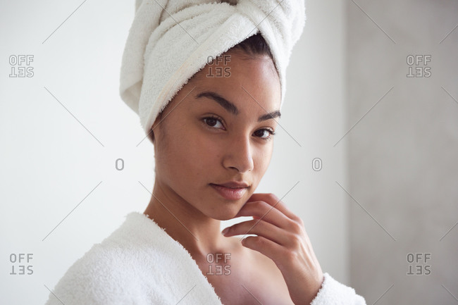 Portrait of mixed race woman spending time at home self isolating and social distancing in quarantine lockdown during coronavirus covid 19 epidemic, wearing bathrobe with towel on her head in bathroom