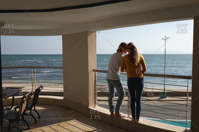 Caucasian couple standing on a balcony, embracing. Social distancing and self isolation in quarantine lockdown.