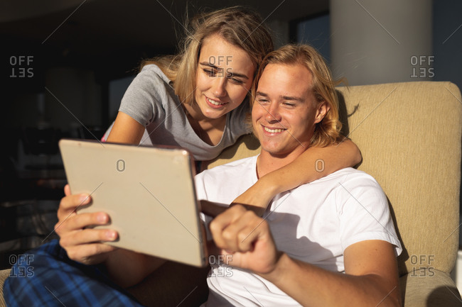 Caucasian couple sitting on a balcony, embracing and using a digital tablet. Social distancing and self isolation in quarantine lockdown.