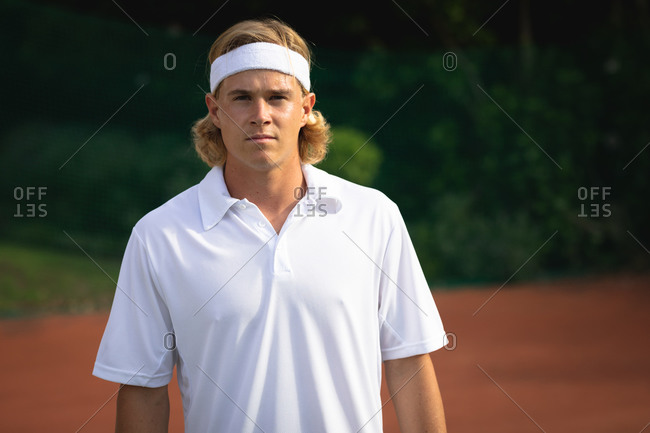 Portrait of a Caucasian man wearing tennis whites spending time on a court playing tennis on a sunny day, looking at camera