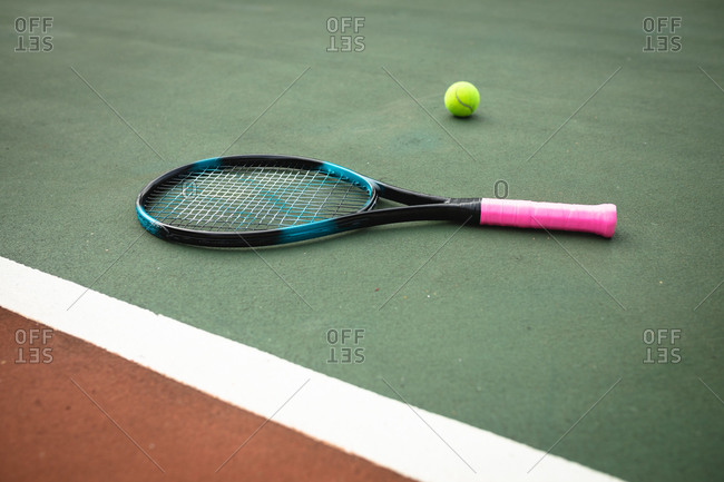 Close up of a tennis racket lying next to a tennis ball on a tennis court on a sunny day