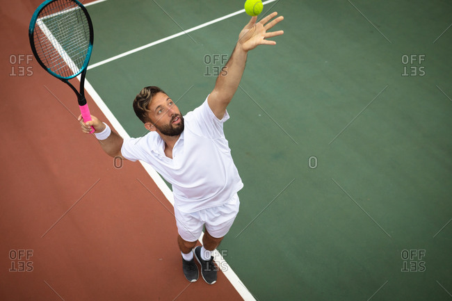 A mixed race man wearing tennis whites spending time on a court playing tennis on a sunny day, preparing to hit a ball