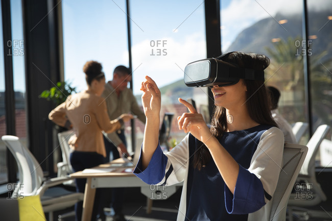 An Asian businesswoman working in a modern office, wearing VR headset, touching virtual interactive screen, with her colleagues working in the background