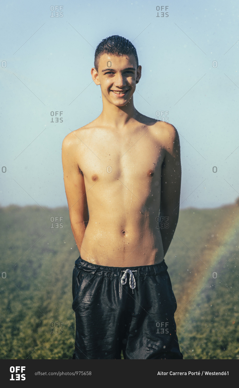 Shirtless teenage boy enjoying sprinkler in farm against clear sky ...