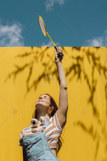 Young woman holding badminton racket over yellow wall during sunny day