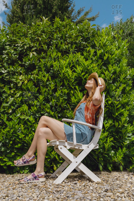 Young woman soaking sunlight while sitting on chair by plant at back yard