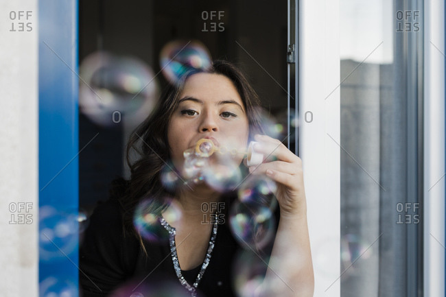 Young woman with down syndrome blowing bubbles from window at home
