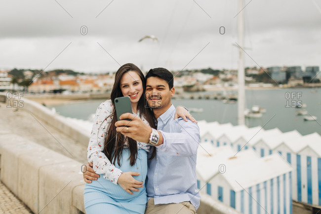 Expectant couple taking selfie through smart phone at harbor- Cascais- Portugal
