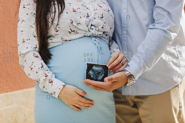Expectant couple holding ultrasound photo while standing outdoors