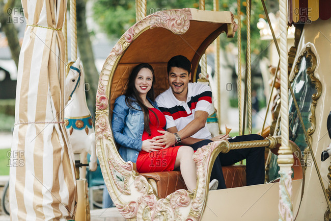 Happy expectant couple sitting on carousel at amusement park- Cascais- Portugal