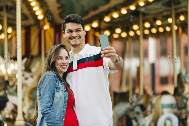 Happy expectant couple taking selfie through smart phone at amusement park- Cascais- Portugal