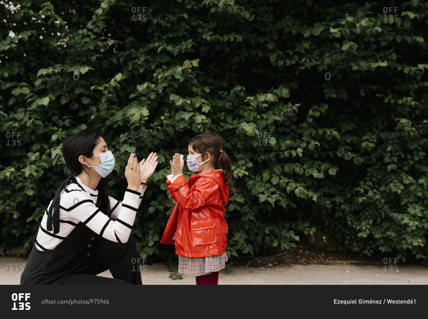 Mother and daughter wearing masks while playing clapping game against plants
