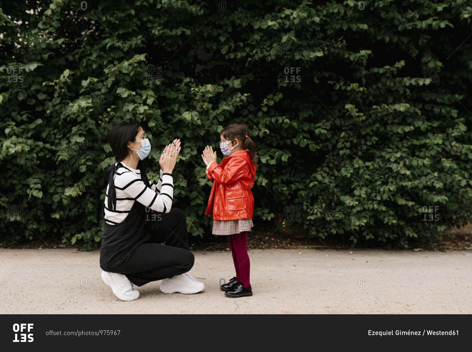 Mother and daughter wearing masks while playing clapping game on street