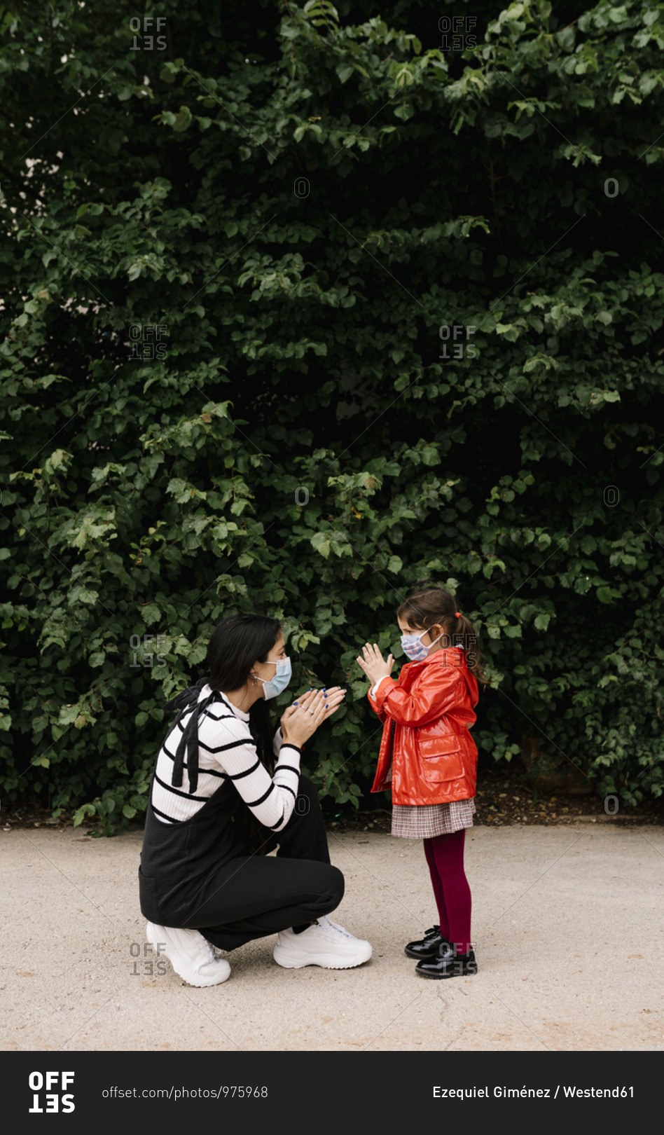 Mother and daughter wearing masks while playing clapping game outdoors