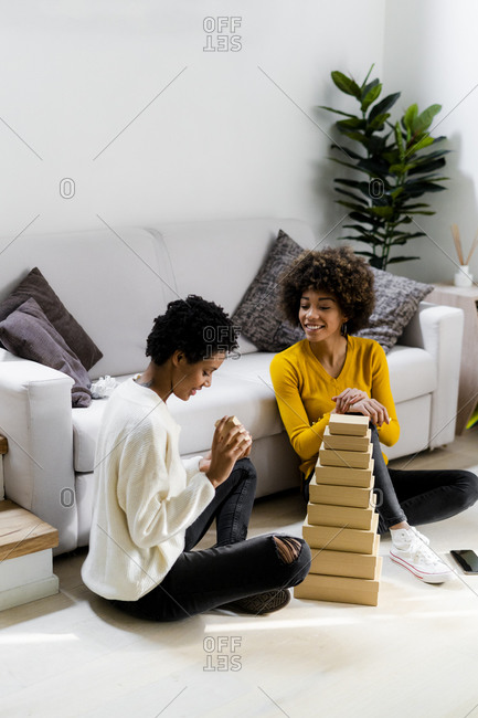 Two young woman sitting on the floor at home stacking boxes in the living room