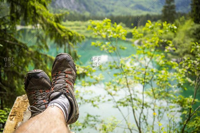 Italy- Province of Udine- Tarvisio- Feet of man wearing hiking boots relaxing on shore of Fusine Lake