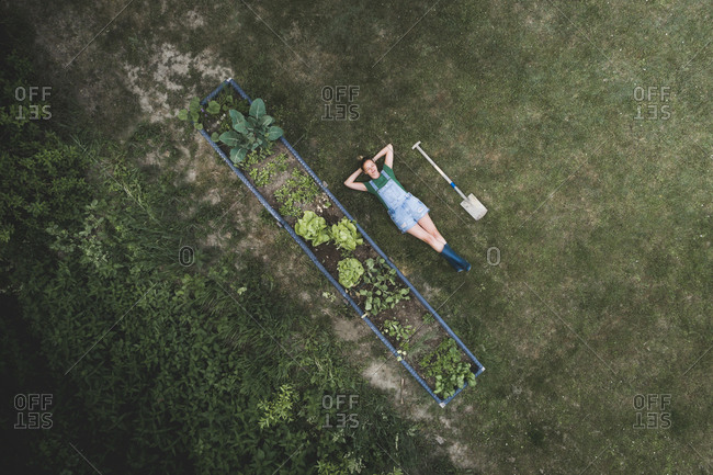 Drone shot of woman with hands behind head lying by raised bed on land