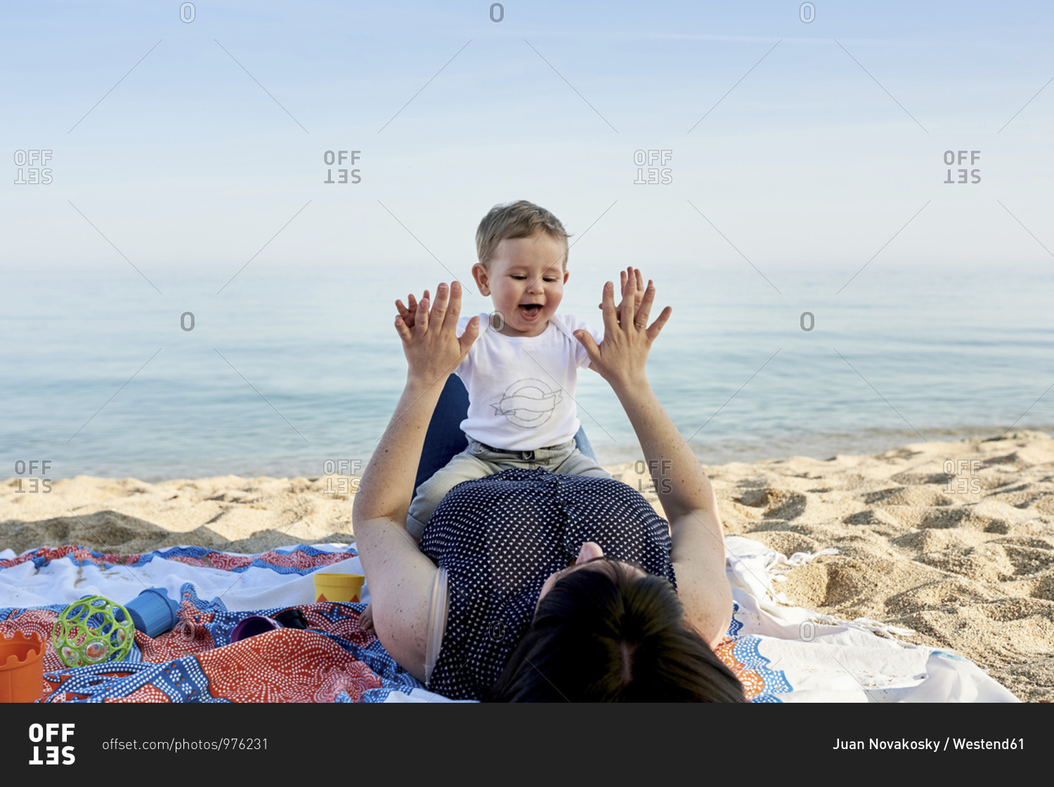 Mother playing clapping game with son while lying on blanket at beach against sea