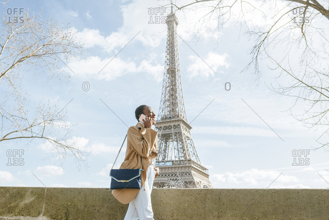 Young woman using smart phone while walking on bridge with Eiffel Tower in background- Paris- France