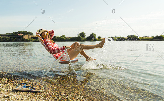 Young woman sitting on deckchair in river splashing with water