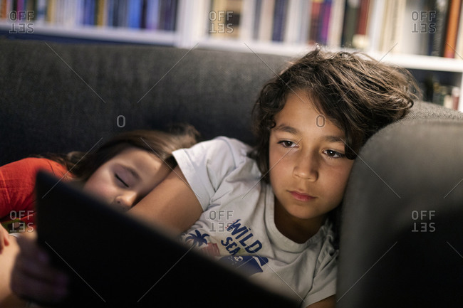 Girl sleeping by brother using digital tablet while relaxing on sofa at home