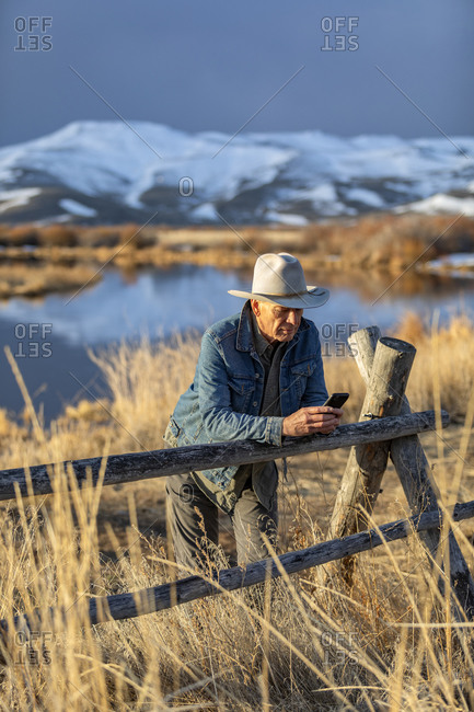 USA, Idaho, Sun Valley, Senior man in cowboy hat leaning against fence