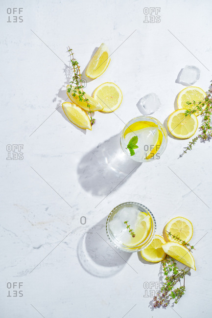 From above glasses with refreshing cold thyme and ginger lemonade with slices of lemon and mint leaves served on table in light room