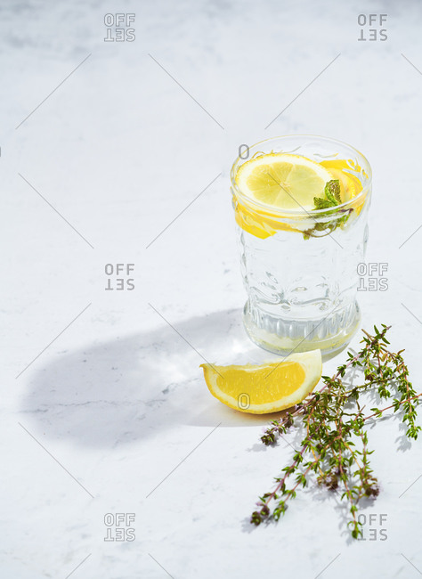 Glasses with refreshing cold thyme and ginger lemonade with slices of lemon and mint leaves served on table in light room