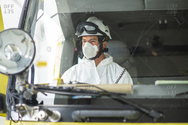 Serious firefighter wearing respirator and helmet sitting in fire car
