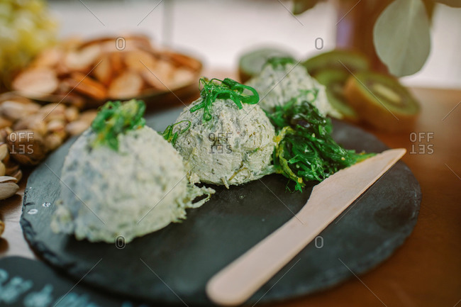 Palatable dish made of cottage cheese garnished with green seaweed and placed on slate board